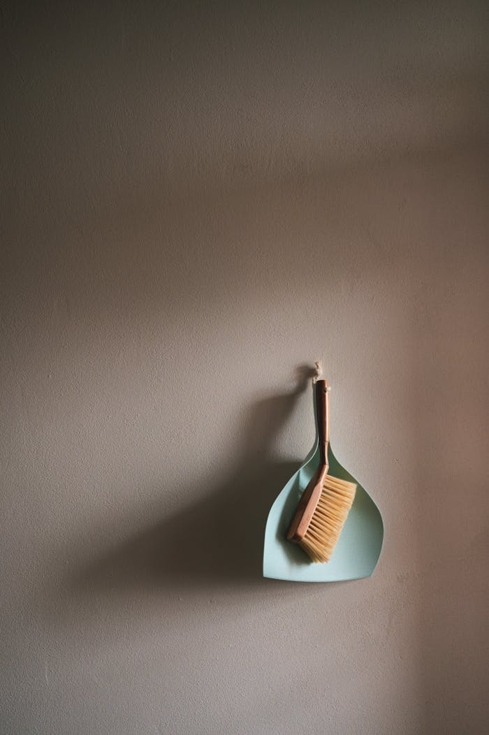 A simple dustpan and brush set hanging against a clean grey wall, perfect for cleaning concepts.